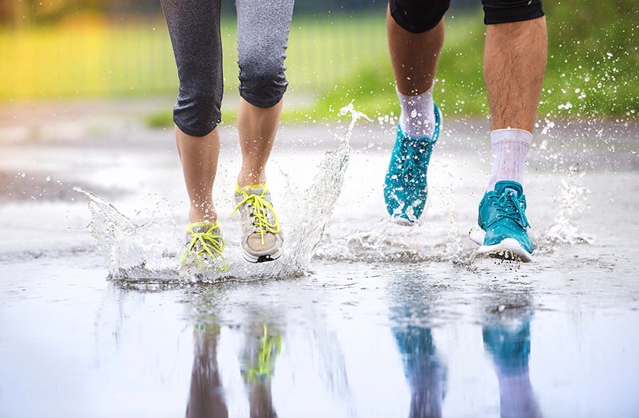 A photo of two people from the legs down, wearing trainers and running through a puddle