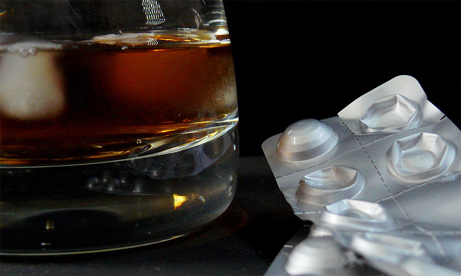 Glass of alcohol with strip of pills on table